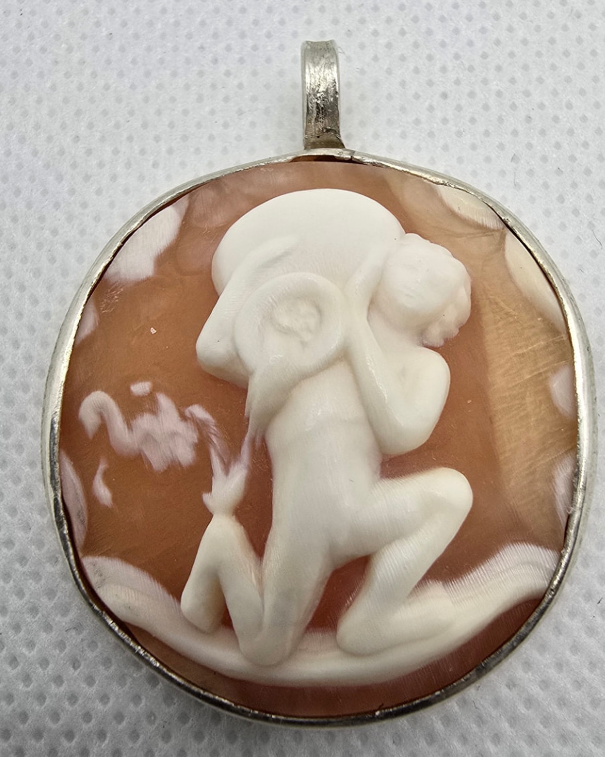 The Wanderer — hand-carved shell cameo showing a reclining figure in a broad hat, in raised white relief against warm reddish-orange shell