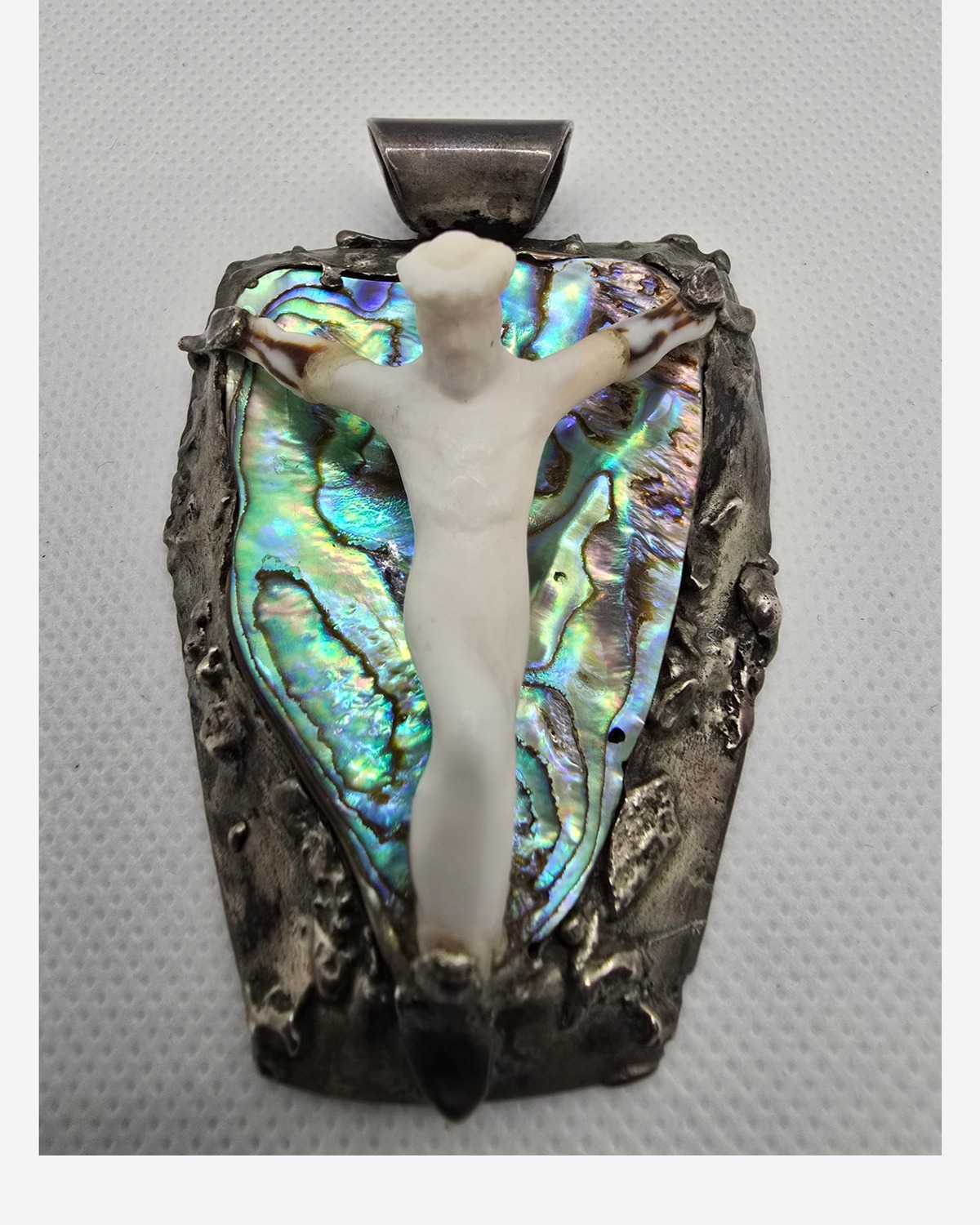 The Crucifixion — hand-carved three-dimensional shell figure of Jesus Christ mounted over an intensely iridescent mother-of-pearl background within a rugged handcrafted silver setting