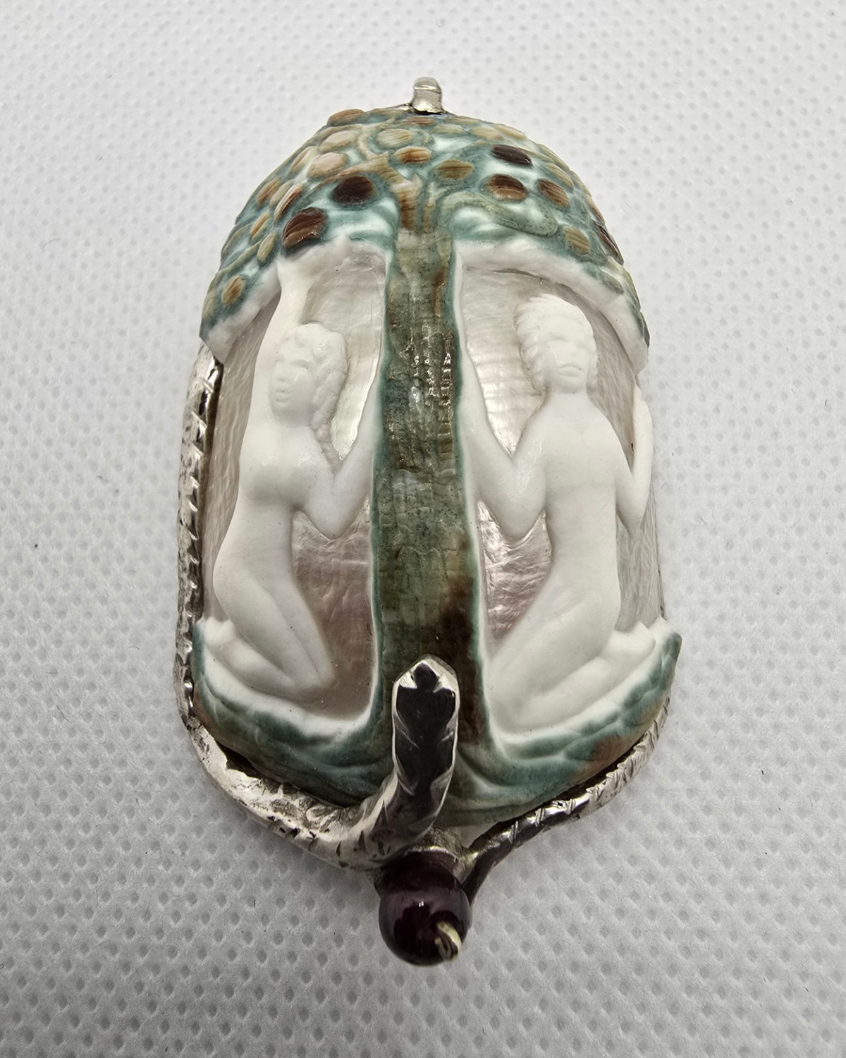 The Garden of Eden — hand-carved sea shell cameo of Adam and Eve seated on either side of the Tree of Knowledge beneath a fruit-filled canopy, in a handmade silver framework