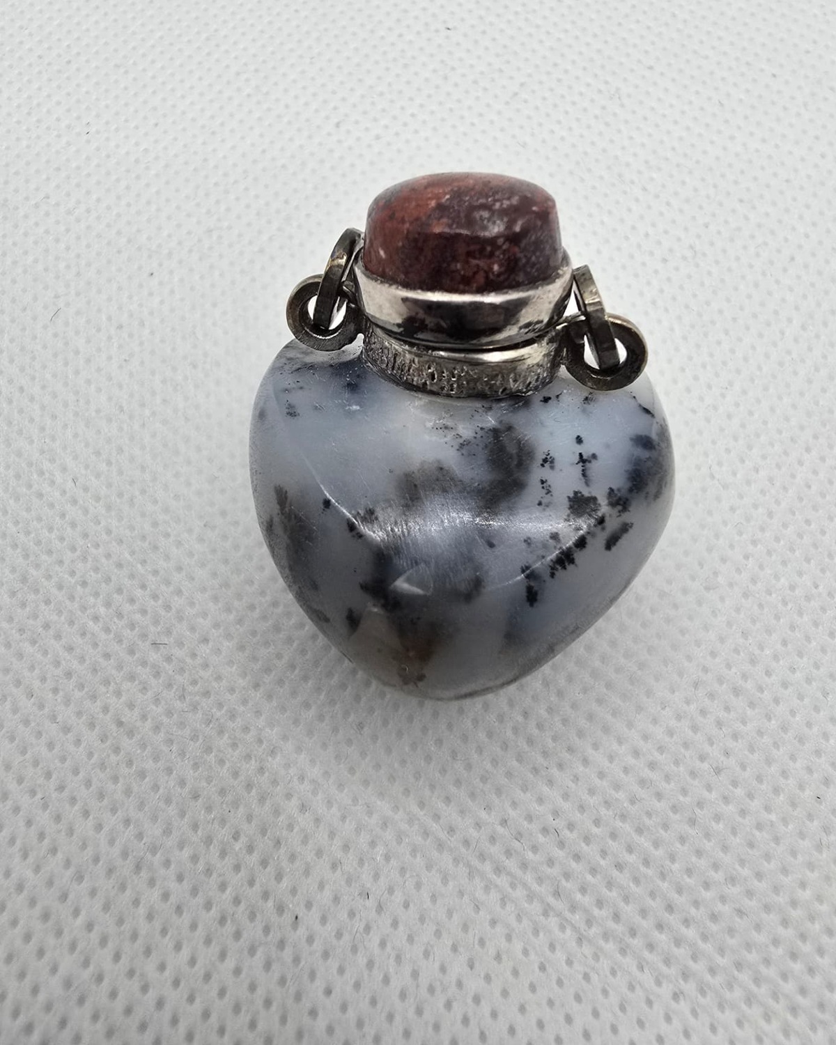 Heart-shaped dendritic agate vessel with silver mount and red cabochon, front view