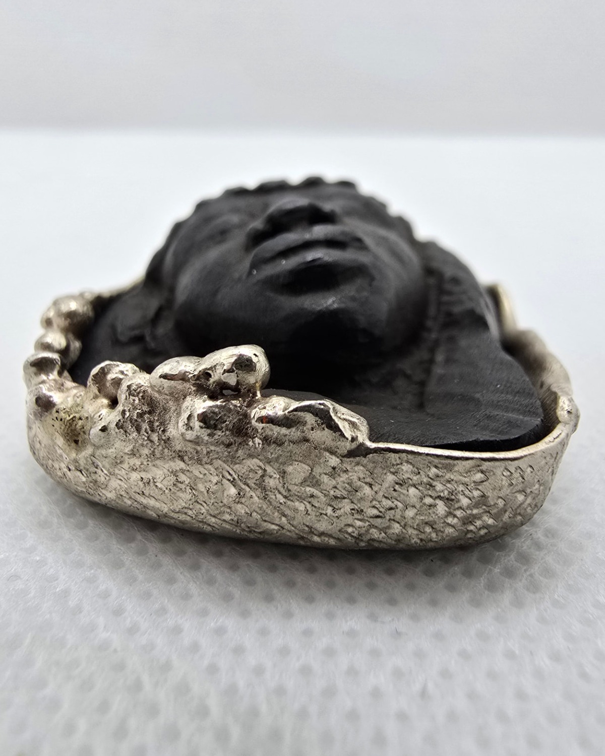 The Daughter of the Earth — low-angle view showing how far the carved face projects from the surrounding jet and silver