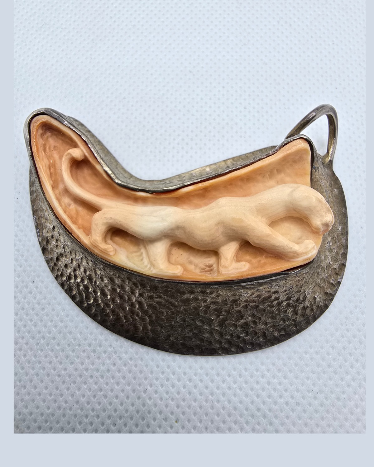 The Crescent — hand-carved sea shell cameo of a striding feline in raised pale relief against warm peach shell, in a hammered crescent surround
