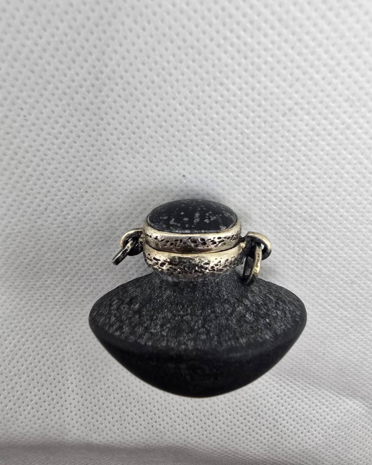 Hand-carved dark stone vessel with silver collar and cabochon stopper, side view