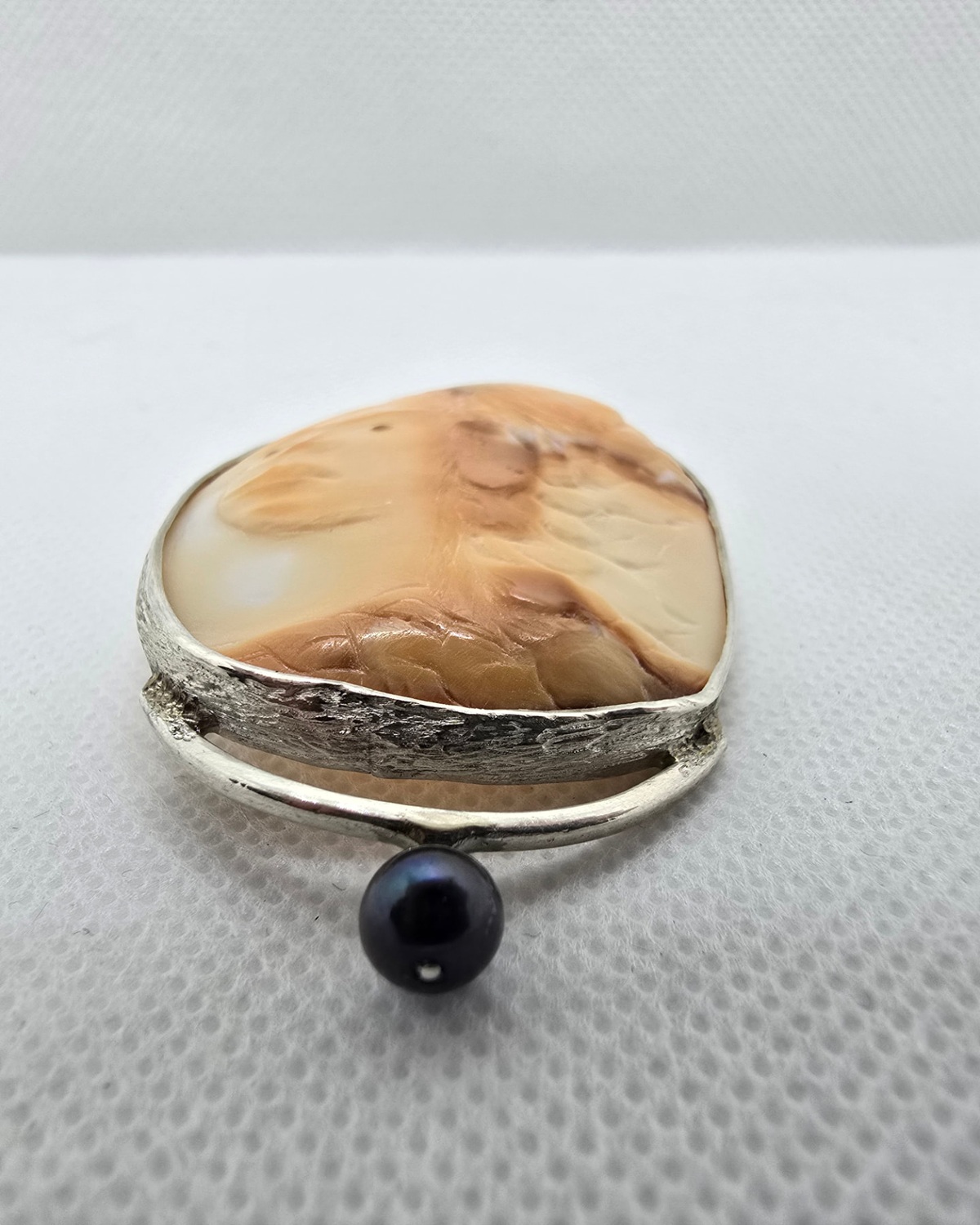 The Guardian — low-angle view showing carving depth, shell thickness, the handmade silver edge and the suspended ornament