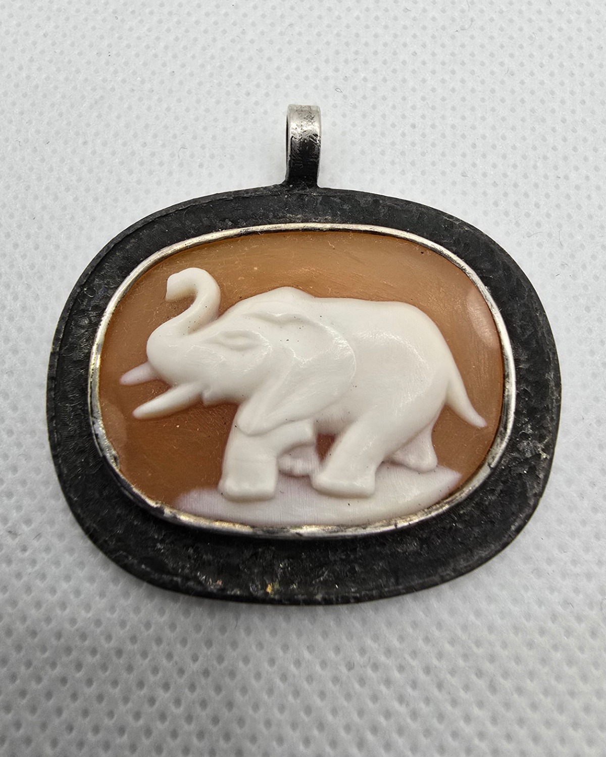 The Elephant of Strength — hand-carved sea shell cameo of an elephant with raised trunk in pale relief against warm orange-brown shell, in a darkened silver pendant frame