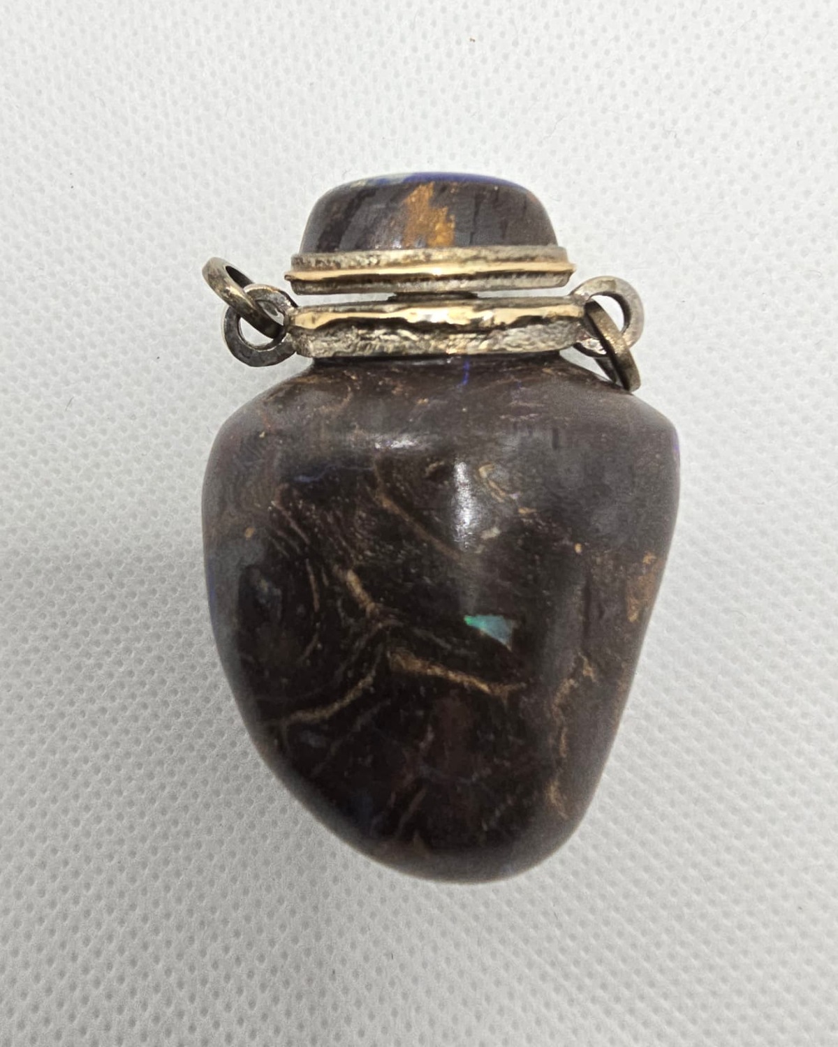Dark boulder opal vessel, angled view showing opal flash