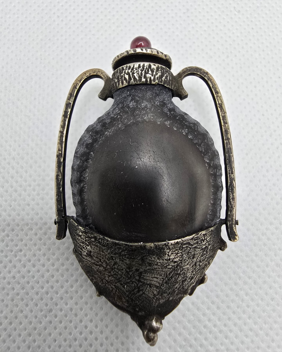 Dark sculptural amphora with silver handles and ruby-red cabochon stopper, front view