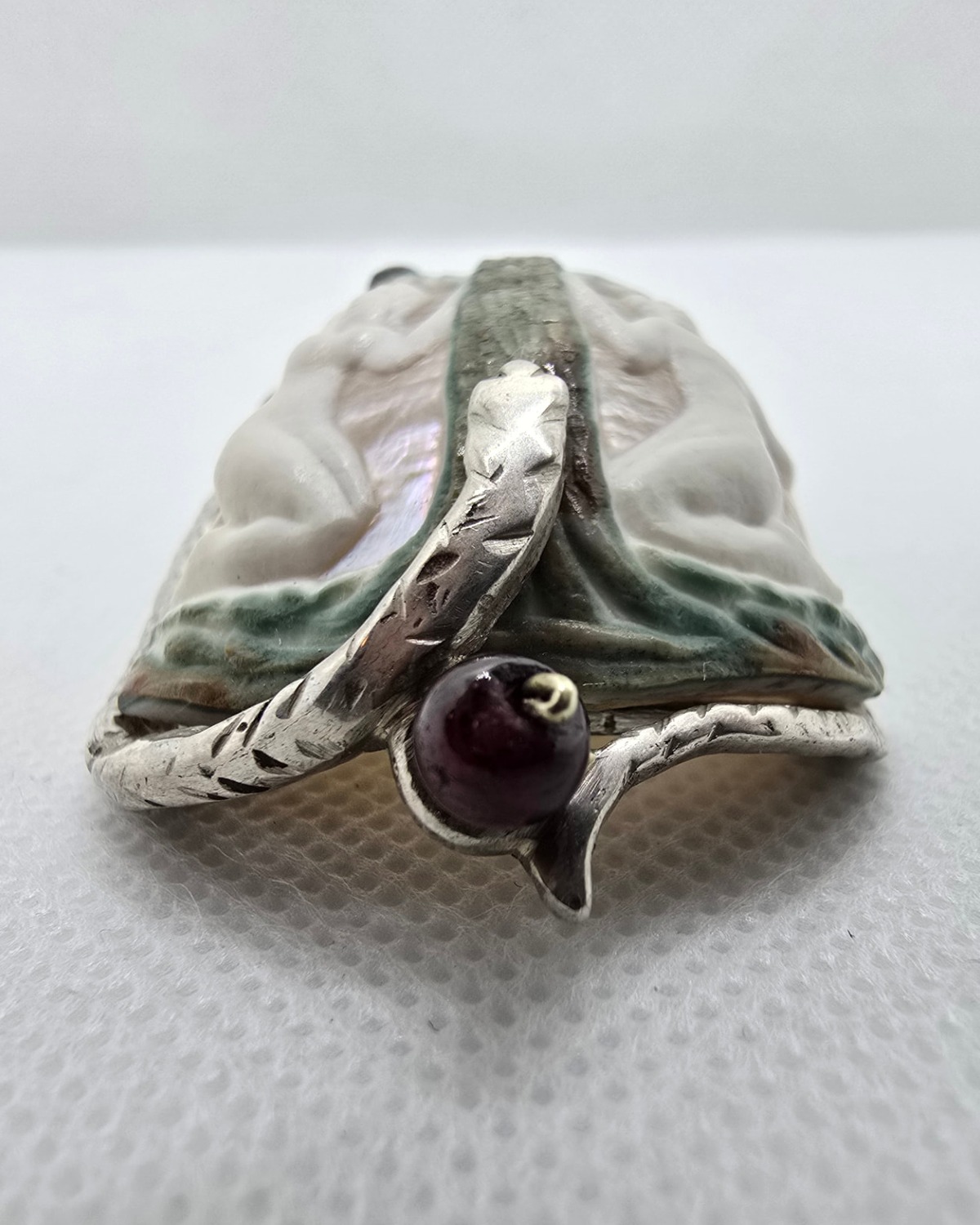 The Garden of Eden — profile view showing the sculptural depth of the carving and the deep red-purple bead held in the silver element at the base