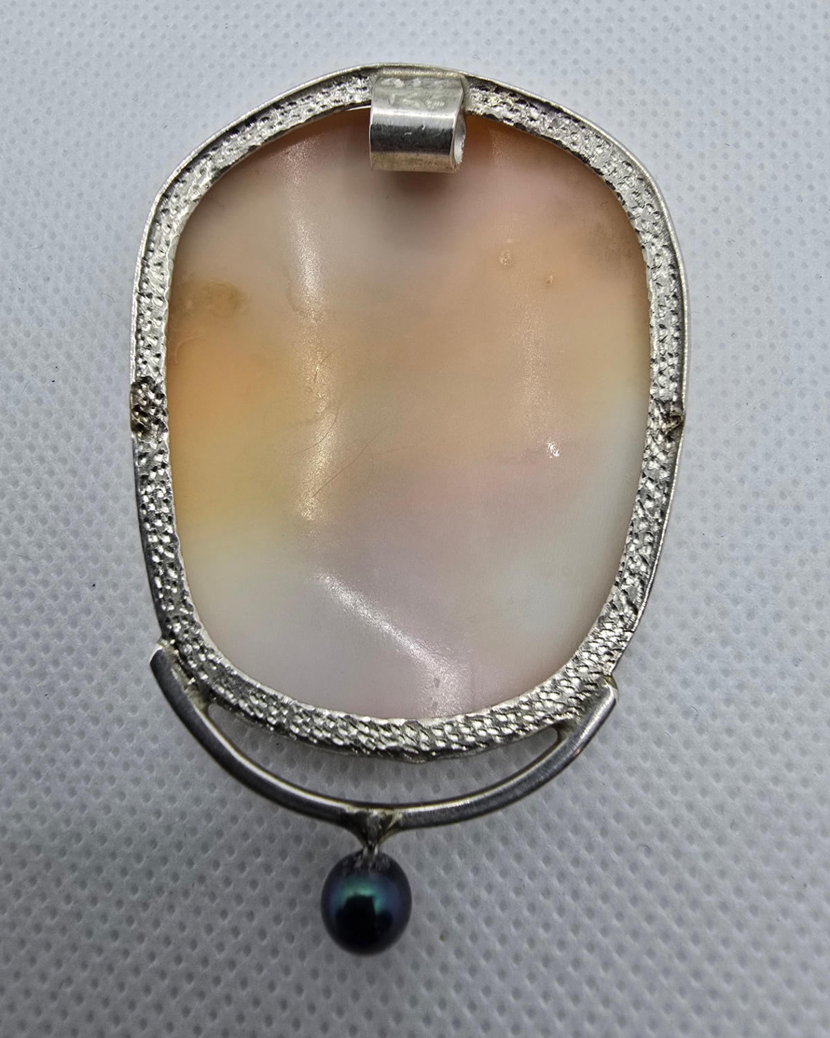The Guardian — reverse showing the natural shell within a textured handmade silver surround, upper bail and suspended dark ornament