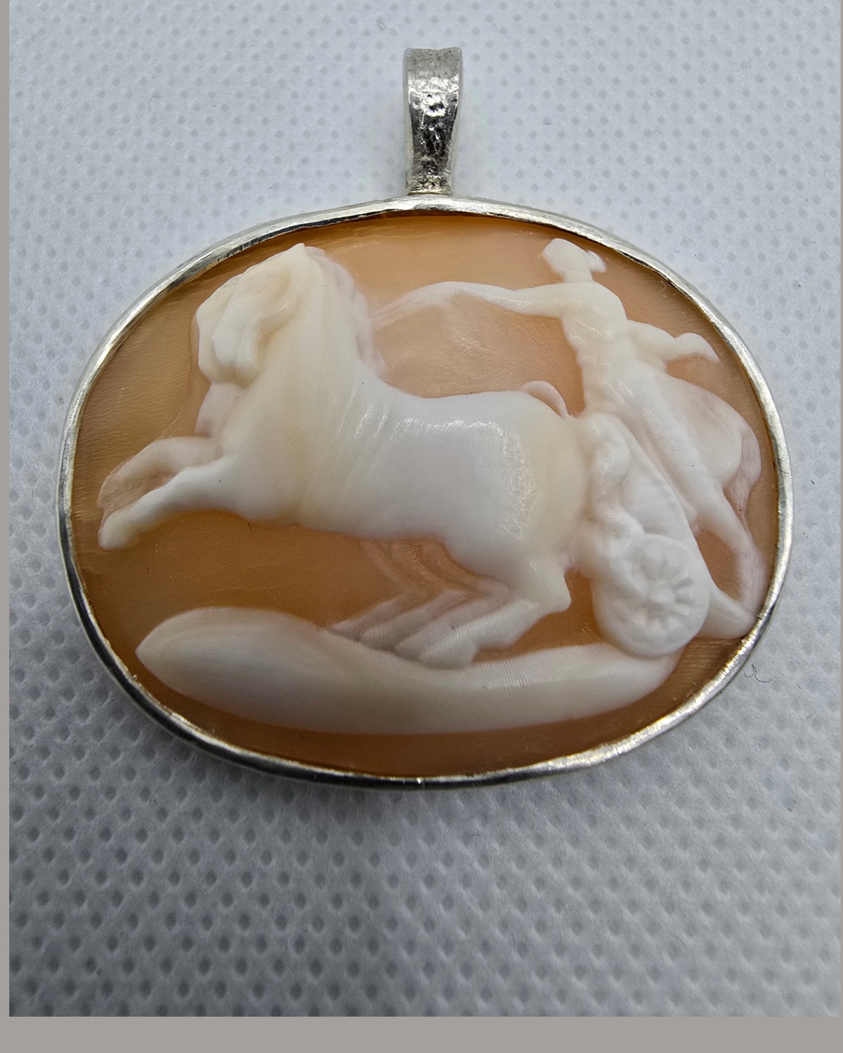 The Chariot of Victory — hand-carved sea shell cameo of a classical chariot scene, with a horse in pale high relief against warm peach-orange shell in a handmade silver pendant frame