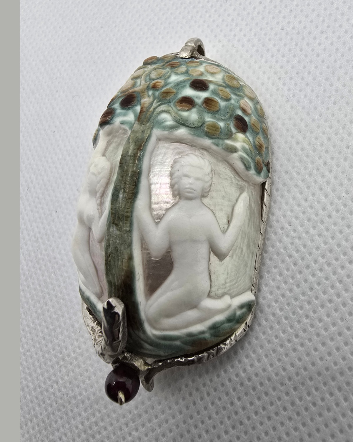 The Garden of Eden — angled view showing one figure in deep relief against luminous mother-of-pearl and the curvature of the carved shell