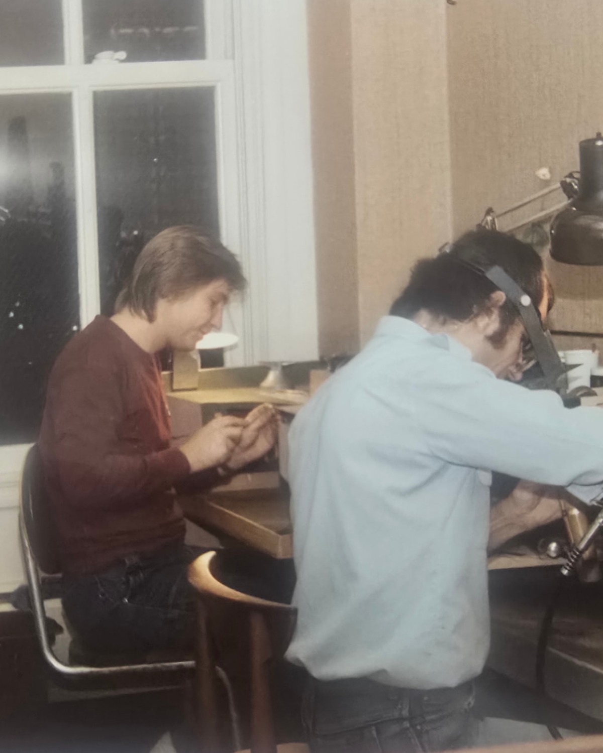 Grzegorz Kiernicki wearing a loupe headband while working at the jeweller's bench beside an apprentice
